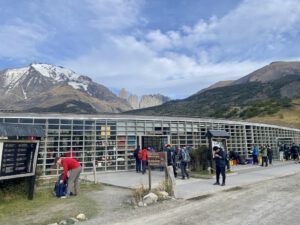 Ein Glasgebäude vor einer Bergkulisse mit blauem Himmel. Davor stehen viele Menschen in Wanderausrüstung.