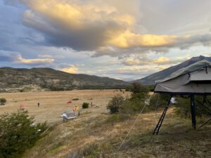 Im Vordergrund ein Zelt auf Stelzen, im Hintergrund eine große Wiese auf der vereinzelt Zelte stehen.